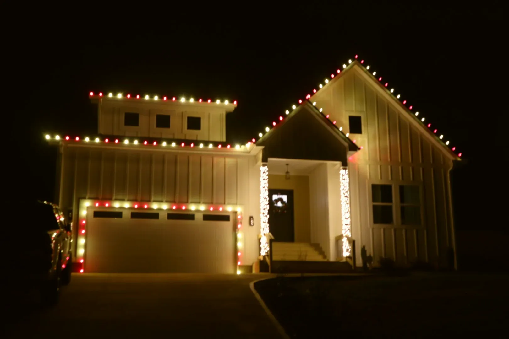 A garage and front porch at night outlined in red and white bulbs.