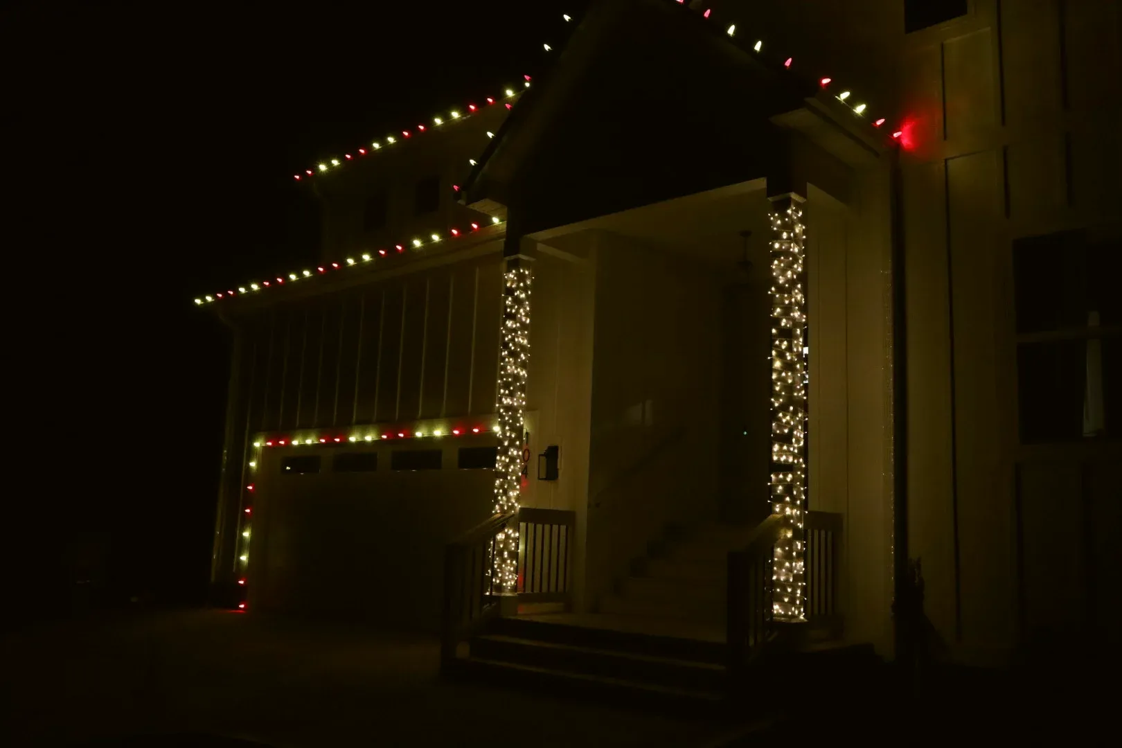 Porch columns wrapped top to bottom in warm white lights, with red and white bulbs along the porch roof.